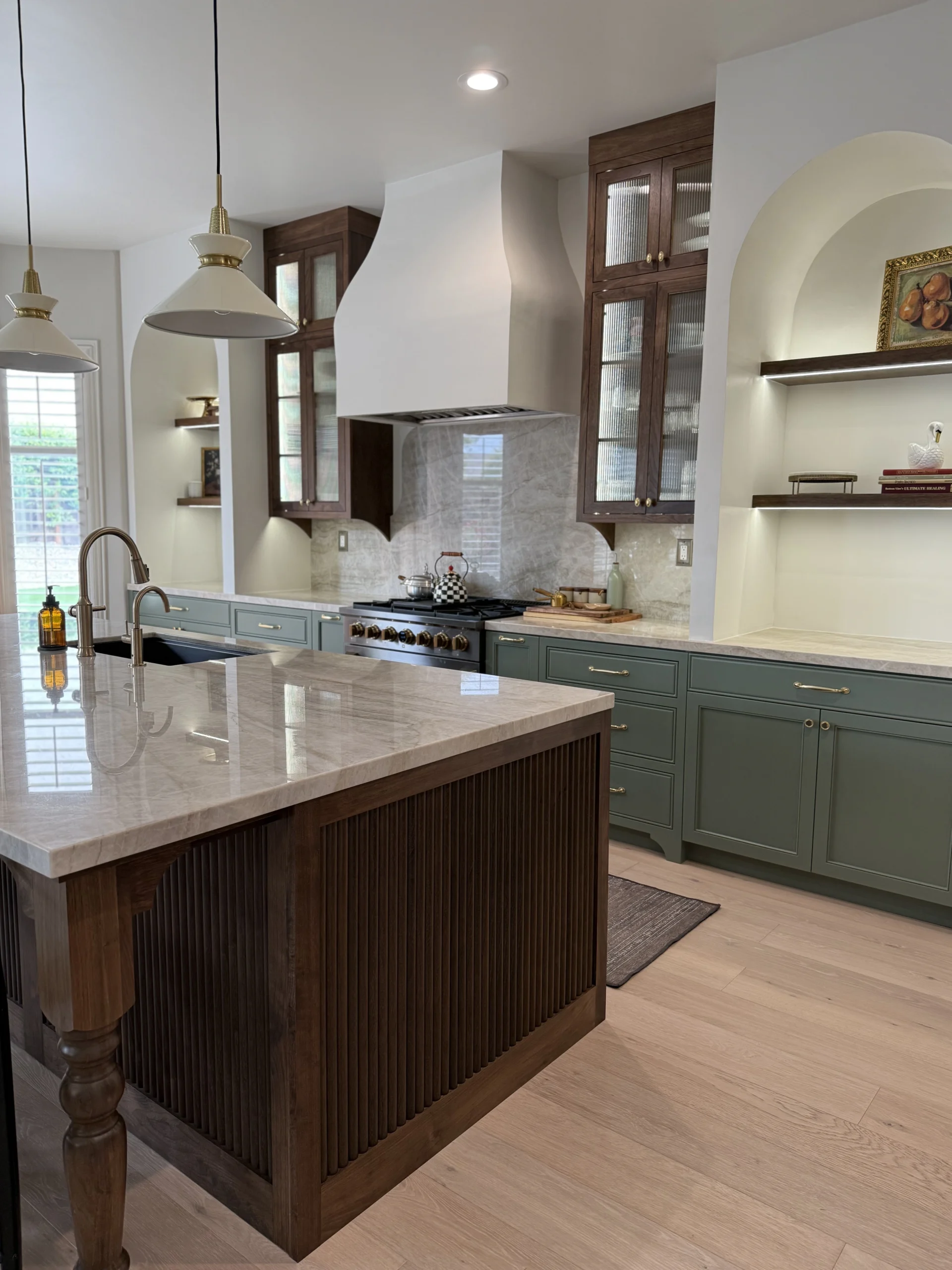 Heirloom-quality custom cabinetry by Anani Remodeling — handcrafted kitchen with sage green cabinets, walnut island, and arched glass-front display cases