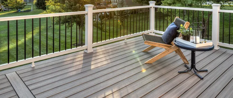 Backyard Trex composite deck with grey board pattern, white posts, and black aluminum baluster railing overlooking a lawn