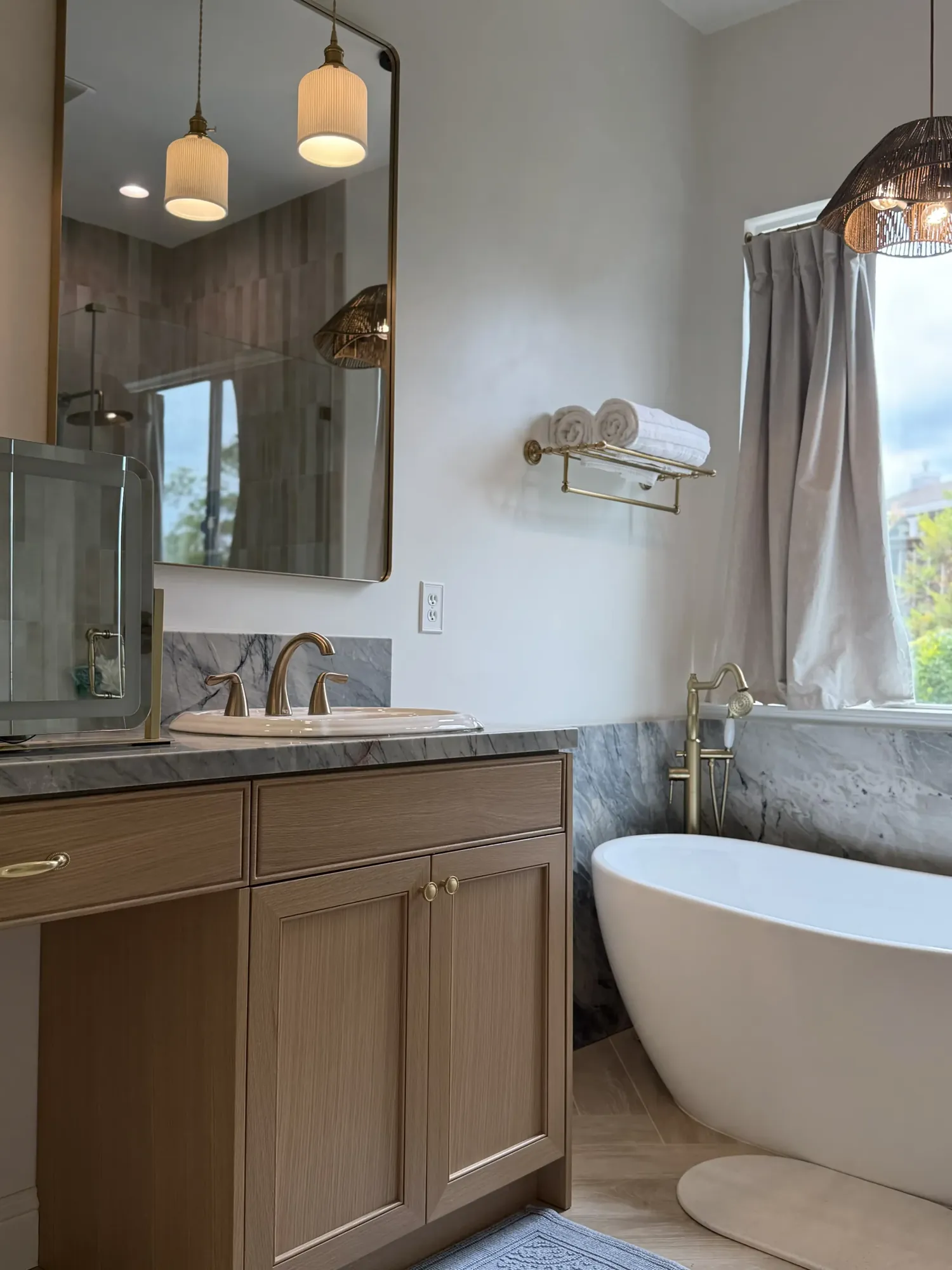 Spa bathroom with arched mirror, marble vanity backsplash, freestanding soaking tub, and woven pendant lights