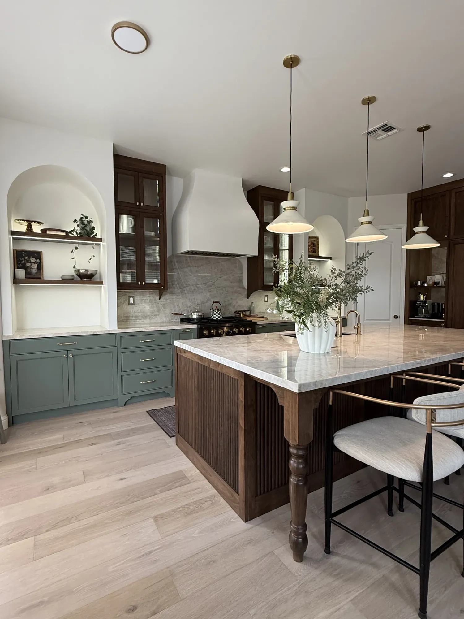 Finished custom kitchen with sage green shaker cabinets, walnut accents, marble waterfall island, and brass pendant lighting